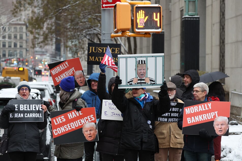 People hold signs outside the Manhattan federal court for the second defamation trial against former US President and 2024 presidential candidate Donald Trump.