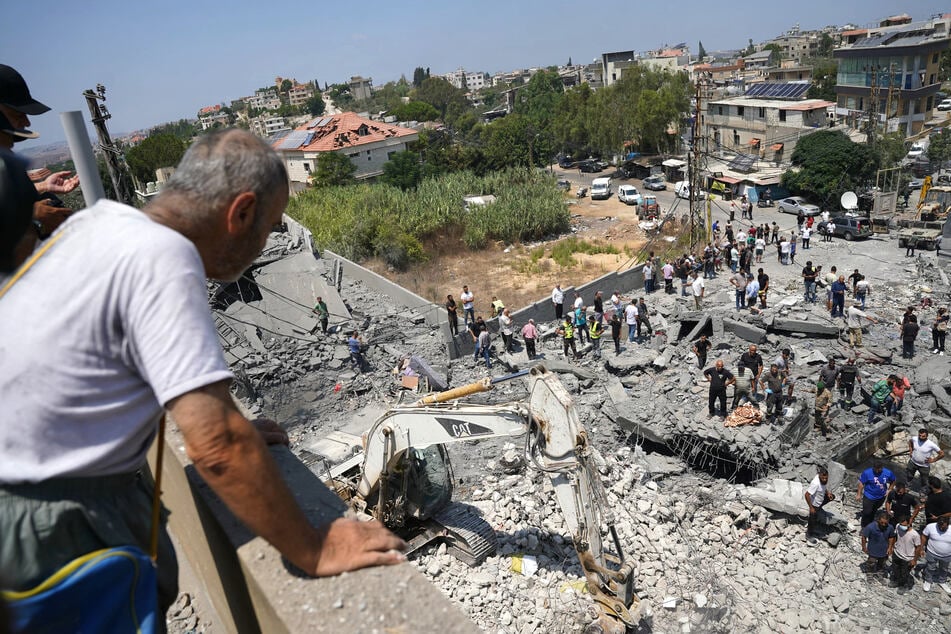 A man watches as heavy machinery, first aid responders, and residents search the site of an Israeli airstrike that targeted a neighborhood in the southern Lebanese village of Deir al-Zahrani on August 15, 2026.