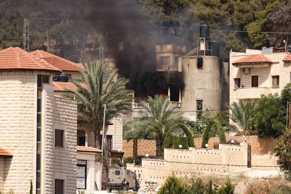 An Israeli military vehicle is parked in front of a building on fire during an Israeli raid in the occupied West Bank city of Jenin.