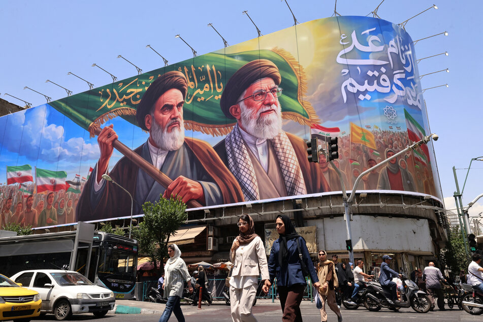 People cross the street past a large billboard showing portraits of Iran's late supreme leader, Ayatollah Ruhollah Khomeini (l.) and slain supreme leader Ayatollah Ali Khamenei (r.) in central Tehran on June 8, 2026.