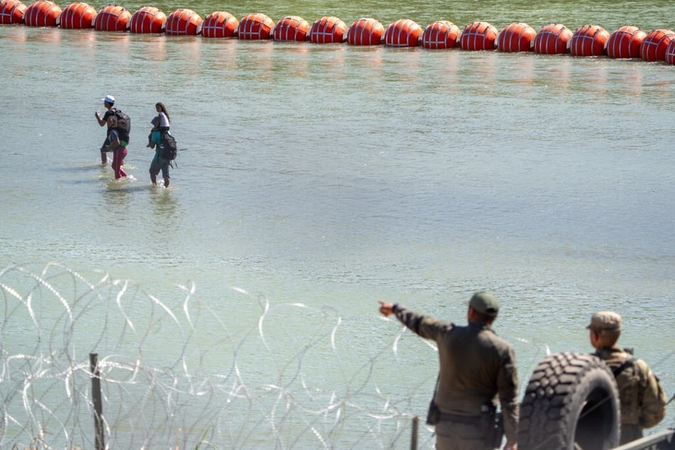 Texas Department of Public Safety highway patrol troopers look over the Rio Grande as migrants walk by a string of buoys placed on the water along the Rio Grande border with Mexico in Eagle Pass, Texas.