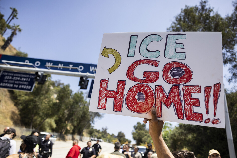 A demonstrator holds a poster reading “ICE Go Home” in front of one of the parking lot entrances at Dodgers Stadium in Los Angeles, California.