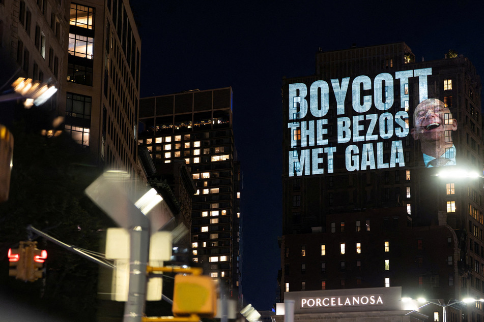 Activists project protest messages highlighting issues of wealth inequality, climate accountability, and labor rights onto the facade of a building which can be seen from Jeff Bezos' penthouse on the eve of the Met Gala.