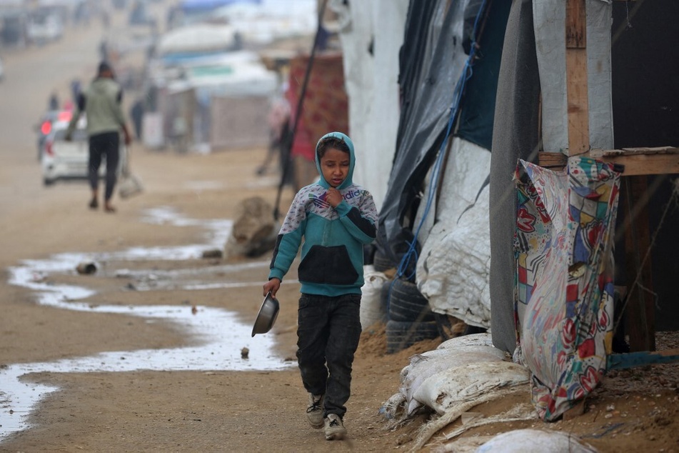 A Palestinian child runs to shelter from the rain at a camp for internally displaced on the beach near the Nuseirat refugee in the central Gaza Strip on December 20, 2024.
